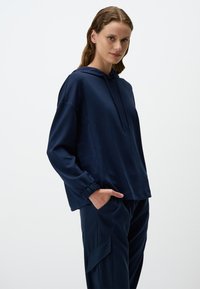 Felpa con cappuccio blu navy, maniche lunghe, polsini elasticizzati e vestibilità rilassata. Abbinata a pantaloni navy coordinati con tasche cargo.