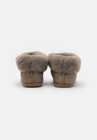 Brune semskede tøfler med en fluffy, lysebrun shearling krave, rund form og diskrete stikninger langs bagsømmen.