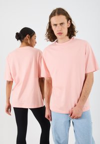 Du pirmininkai vilki per didelius, trumpomis rankovėmis, šviesiai rožinius medvilninius marškinėlius. Vienas turi juodas leggins, kitas - mėlynas džinsines kelnes.