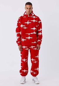 Rode hoodie en sweatpants set met een gedurfde witte sterrenprint. Gemaakt van textuurstof met een ontspannen pasvorm en cuffs bij de enkels.