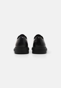 Scarpe in pelle nera con finitura liscia, punta arrotondata, suola in gomma a profilo basso e design posteriore minimalista con piccoli accenti di colore.