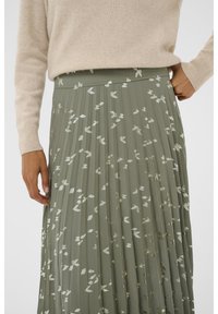 Gonna plissettata in tessuto verde tenue con motivi a foglia metallica. Presenta una vita alta e un drappeggio morbido. La texture sembra leggera.