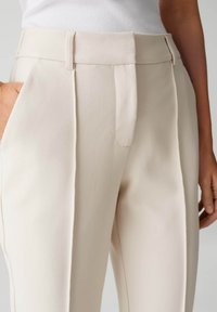 Beige op maat gemaakte broek met een gladde textuur, geplooide voorkant, zijzakken en een aangesloten taille met riemlussen.
