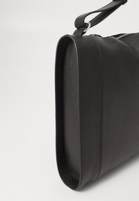 Black textured leather shoulder bag with silver ring and zipper closure, shown from a close side angle on white background.