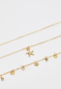 Collier en métal doré à couche avec un pendentif en forme d'étoile de mer et de petites accents circulaires avec des cristaux intégrés, sur une chaîne délicate.