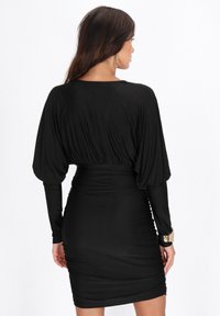 Rochie neagră cu o siluetă ajustată, mâneci lungi și o textură pliată. Spatele are o finisare netedă, cu o lungime până la mijlocul coapsei.