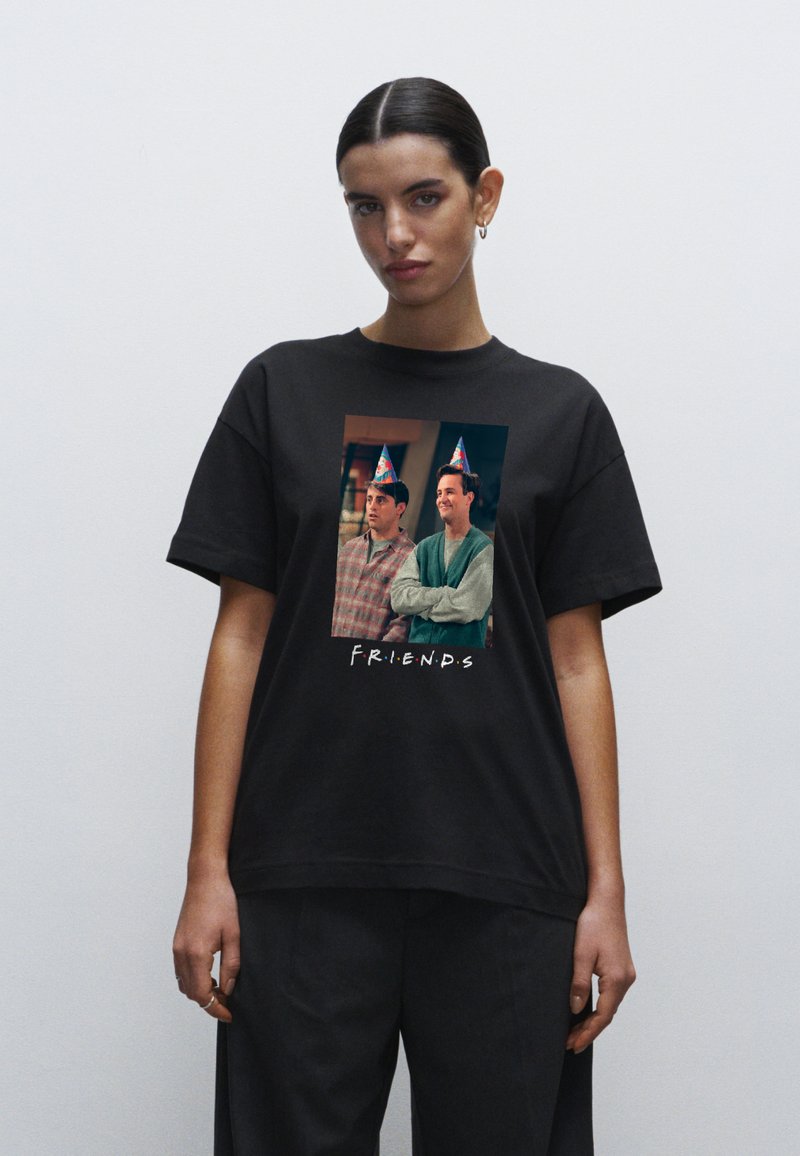 Černé bavlněné tričko s potiskem dvou postav v party kloboucích, s nápisem "F.R.I.E.N.D.S" v bílém textu pod nimi.