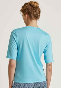 Lichtblauw t-shirt met korte mouwen en een ronde hals, gemaakt van gladde stof. Heeft een zoomlijn die op de taille is gesneden, gedragen met een gestreepte onderkant.