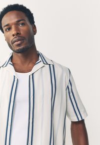 Chemise à manches courtes en tissu léger, présentant des rayures verticales bleues et blanches, fermeture à boutons sur le devant, et un col classique.