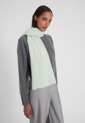 Licht mintgroene sjaal om de nek gewikkeld, gemaakt van zacht stof, gecombineerd met een gestructureerde grijze trui en lichtgrijze broek.