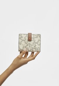 Cream-colored wallet with a textured pattern, featuring a brown snap closure and a smooth finish, held in a hand against a light background.