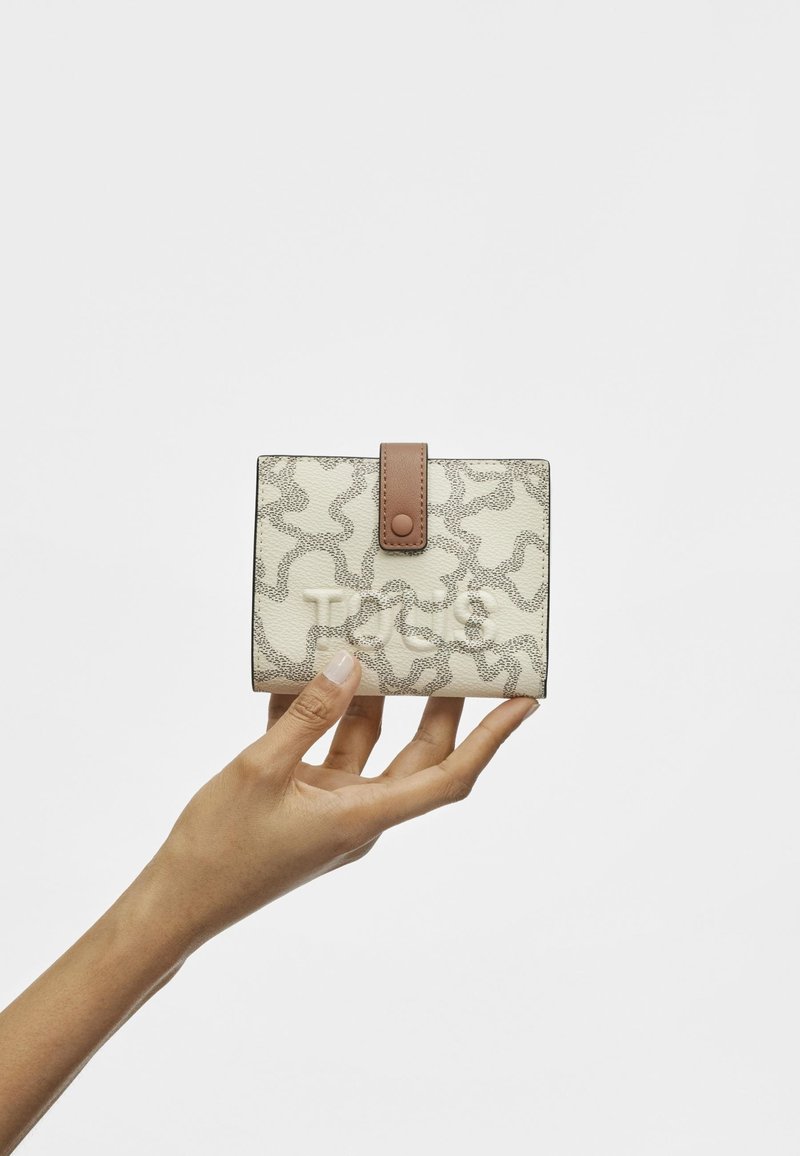 Cream-colored wallet with a textured pattern, featuring a brown snap closure and a smooth finish, held in a hand against a light background.