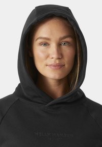 Černá mikina s kapucí a jemnou texturou, na přední straně zdobená embosovaným logem "Helly Hansen", navržena pro pohodlí a volný čas.