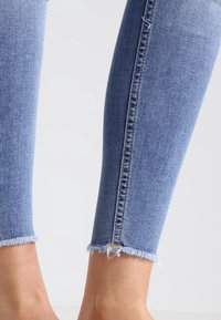 Jeans skinny de denim azul claro, con dobladillo deshilachado, diseño ajustado y sutilezas de costura a lo largo del costado.