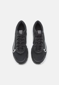 Chaussures de sport noires avec un dessus en maille texturée, bout rond, accents blancs et lacets noirs. Présente un logo sur la languette.