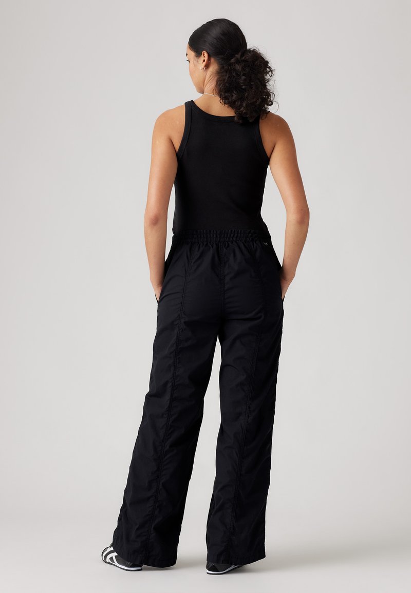 Schwarzes geripptes Tanktop kombiniert mit lockeren, leichten schwarzen Hosen mit elastischem Bund und seitlichen Taschen.