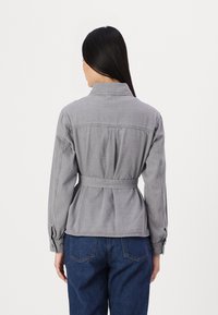 Grå denimjacka med bälte i midjan, knäppta ärmar och en lätt rynkad detalj bak. Stylad med blå denimbyxor.