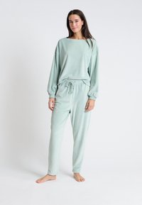 Ensemble de détente à fines côtes vert clair comprenant un haut à manches longues à coupe ample et un pantalon à taille élastique avec cordon de serrage. Texture douce sur l'ensemble.