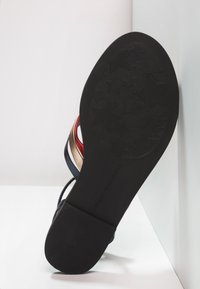 Semelle de sandale montrant un motif d'étoiles sur la bande de roulement et le talon, avec des sangles rouges, dorées et bleu marine partiellement visibles.