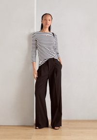 Gestreiftes Langarmoberteil in Schwarz und Weiß, kombiniert mit hochtaillierten schwarzen Hosen. Das Outfit zeichnet sich durch eine lockere Passform und minimale Details aus.