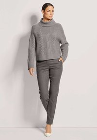Grauer gestrickter Rollkragenpullover mit Kabelmuster, cropped Fit, kombiniert mit dunkelgrauen maßgeschneiderten Hosen und weißen spitzen Pumps.
