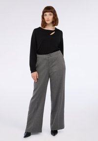 Černý top s dlouhým rukávem a výřezem, doplněný šedými kalhotami s houndstooth vzorem a širokými nohavicemi. Obuv má černé špičaté špičky.