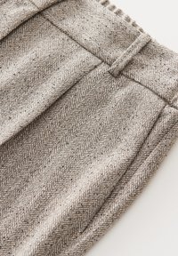 Pantalon gris en tweed taille haute avec passants de ceinture et motif en chevrons, présenté plié sur un fond blanc.