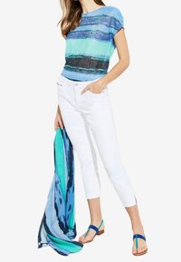 Blusa a rayas azul y turquesa, pantalones cortos blancos y una bufanda estampada, complementados con sandalias de tira verde y azul.