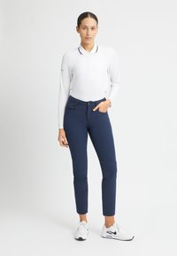 Vit långärmad polo med svart krage och knappar, kombinerad med marinblå byxor och vita sneakers. Minimalistisk design, slät textur.