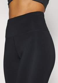 Korkeavyötäröiset mustat leggingsit sileästä, joustavasta kankaasta, saumattomalla muotoilulla ja huomaamattomilla ompelusyillä vyötäröllä ja sivuilla.