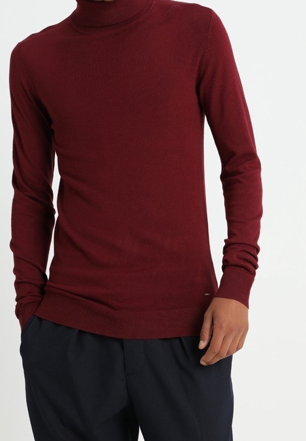 Maglione a collo alto di color bordeaux realizzato in morbido tessuto a maglia, con maniche lunghe e una silhouette aderente, abbinato a pantaloni blu scuro.