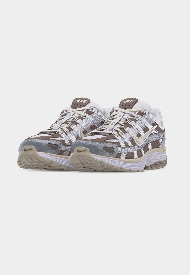 Paire de chaussures de course Nike en beige, blanc et gris avec détails en mesh et en daim, lacets noués, placées côte à côte sur un fond blanc.