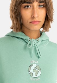 Mint green hoodie in soft material, featuring an embroidered globe graphic with “RVCA” and “LOVE HER” text. Drawstring hood with metal accents.