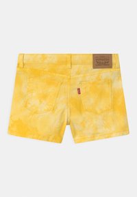 Żółte dżinsowe szorty z wzorem tie-dye, dwoma tylnymi kieszeniami i metką z logo Levi's na pasie. Gładka tekstura, casualowy design.