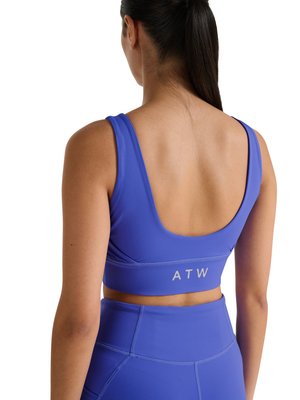 Kvinde med mørkt hår i en hestehale iført en blå sports-bh og høj-taljede leggings, set bagfra, med "ATW" på bh'ens bånd.