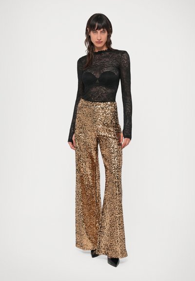 Must mustriba pikkade varrukatega tops, millel on sakiline kaelus, on kombineeritud kuldsete sädelevate laia säärega püksidega, millel on läikiv peegeldav tekstuur.