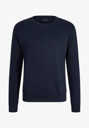 Granatowa bluza z długim rękawem i okrągłym dekoltem, połączona z jasnoszarymi zwężającymi się dresami oraz czarnymi sneakersami. Swobodny zestaw odzieży sportowej.