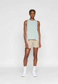 Ανοιχτό πράσινο αμάνικο αθλητικό τοπ με άνετη εφαρμογή, σε συνδυασμό με μπεζ σορτς ποδηλασίας. Περιλαμβάνει διακριτικές λεπτομέρειες λογοτύπου και στα δύο ρούχα.