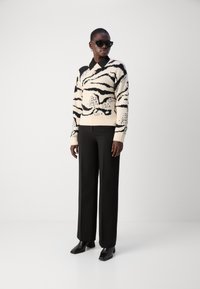 Strickpullover in Creme mit schwarzen Zebra-Streifen, mit V-Ausschnitt und langen Ärmeln; kombiniert mit schwarzen weiten Hosen und eleganten schwarzen Stiefeln.