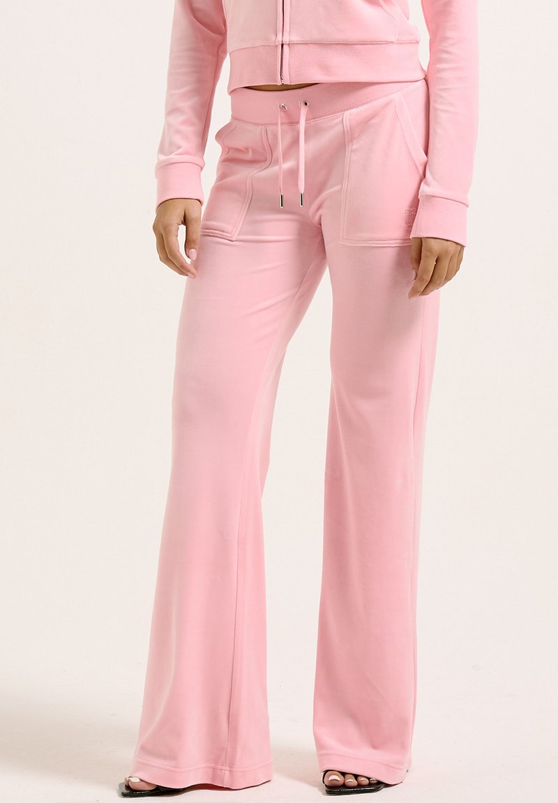 Pantalons de survêtement roses évasés en tissu doux et extensible. Dotés d'une taille à cordon de serrage et de poches avant. Texture lisse, design décontracté.