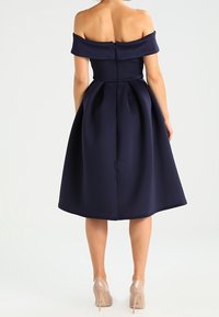 Marinblå off-shoulder-klänning med en figurnära bodice och utsvängd kjol, texturerad tyg och en dragkedja i ryggen. Bärs med nakna klackar.