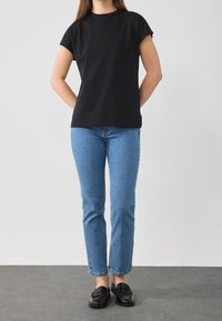 T-shirt nera in cotone con maniche corte, abbinata a jeans azzurri a gamba dritta. Mocassini neri completano l'outfit. Design semplice, dettagli minimi.