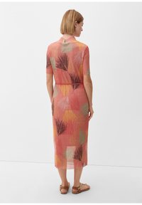 Vestido largo hasta la rodilla, transparente, en color coral con patrones geométricos de hojas en verde, amarillo y negro; presenta mangas cortas y un acento de cintura ajustada.