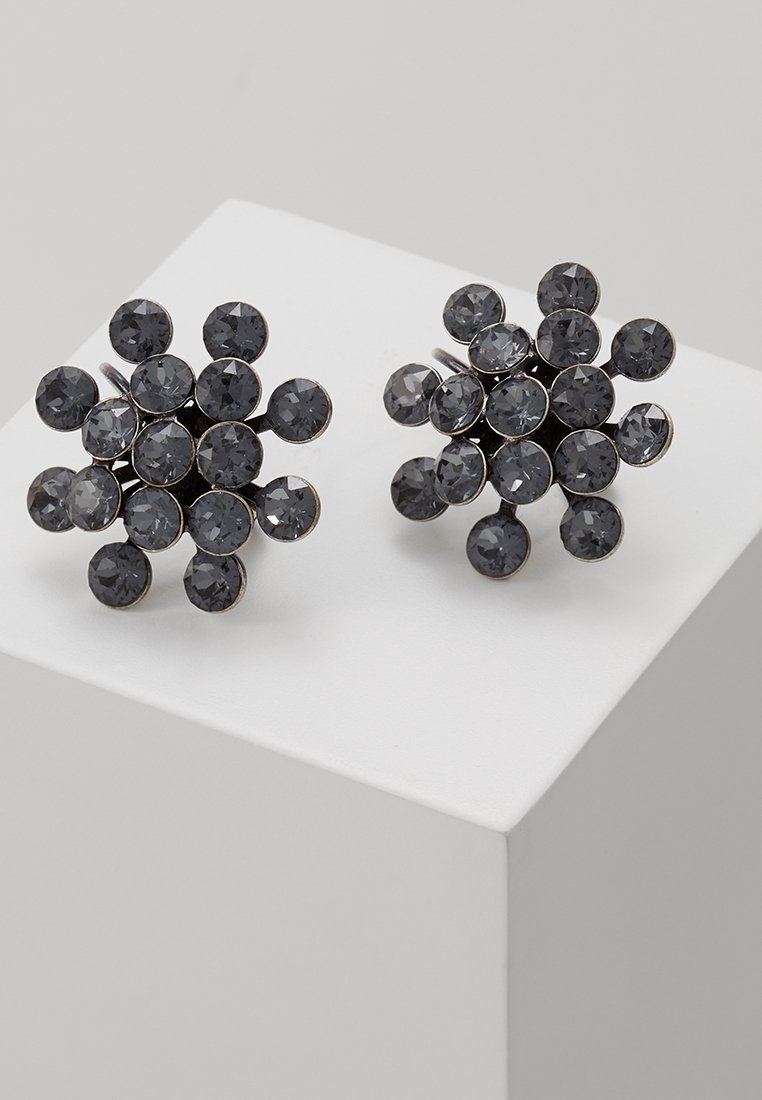 Paire de boucles d'oreilles rondes en grappe comportant plusieurs pierres facettées gris foncé disposées en motif floral sur une surface blanche.
