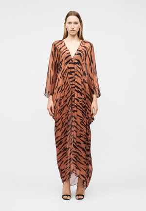 Mujer vistiendo un vestido largo, suelto y transparente de color marrón con rayas negras de tigre y un profundo escote en V, combinado con tacones abiertos negros.