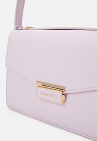 Liliowa torebka syntetyczna z złotym zapięciem i wytłoczonym detalem "ANNA FIELD". Gładka struktura, prostokątny kształt, z klapką zamykającą.