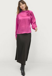 Roze satijnen blouse met lange mouwen en een hoge halslijn, voorzien van drie stoffen rozen op de linker schouder. Gecombineerd met een zwarte, vloeiende rok.