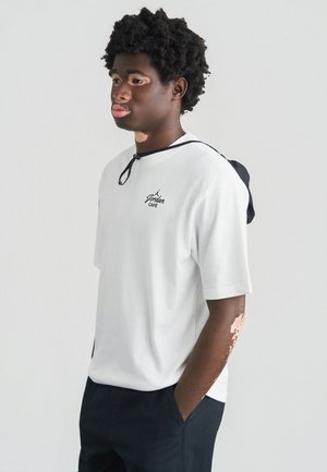 Camiseta blanca de manga corta con cordón negro, con un logo negro de "Jordan Café". El modelo lleva pantalones oscuros. Diseño simple.