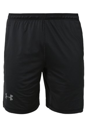 Homme portant un t-shirt de sport blanc à manches courtes, un short de sport noir et des baskets blanches, debout sur un fond gris clair.