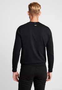 Černá mikina s dlouhými rukávy a žebrovanými manžetami. Na zadní částí výstřihu se nachází malé bílé logo. Měkká tkanina, klasický střih.